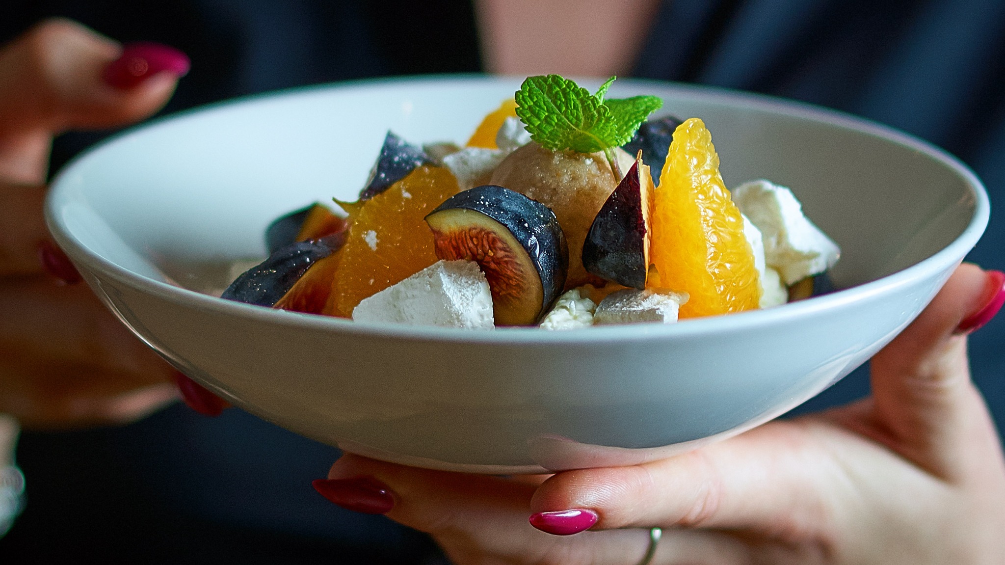 Dessert aux figues et agrumes tenu par une serveuse.