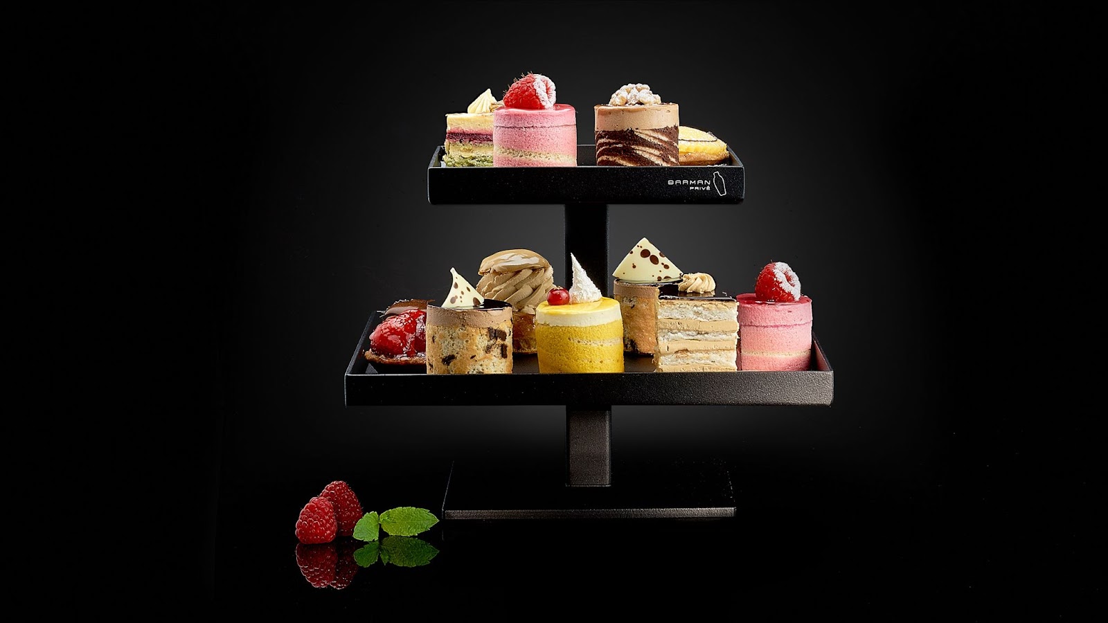 Assortiment de mignardises et petits gâteaux présentés sur un support noir, sur fond sombre.