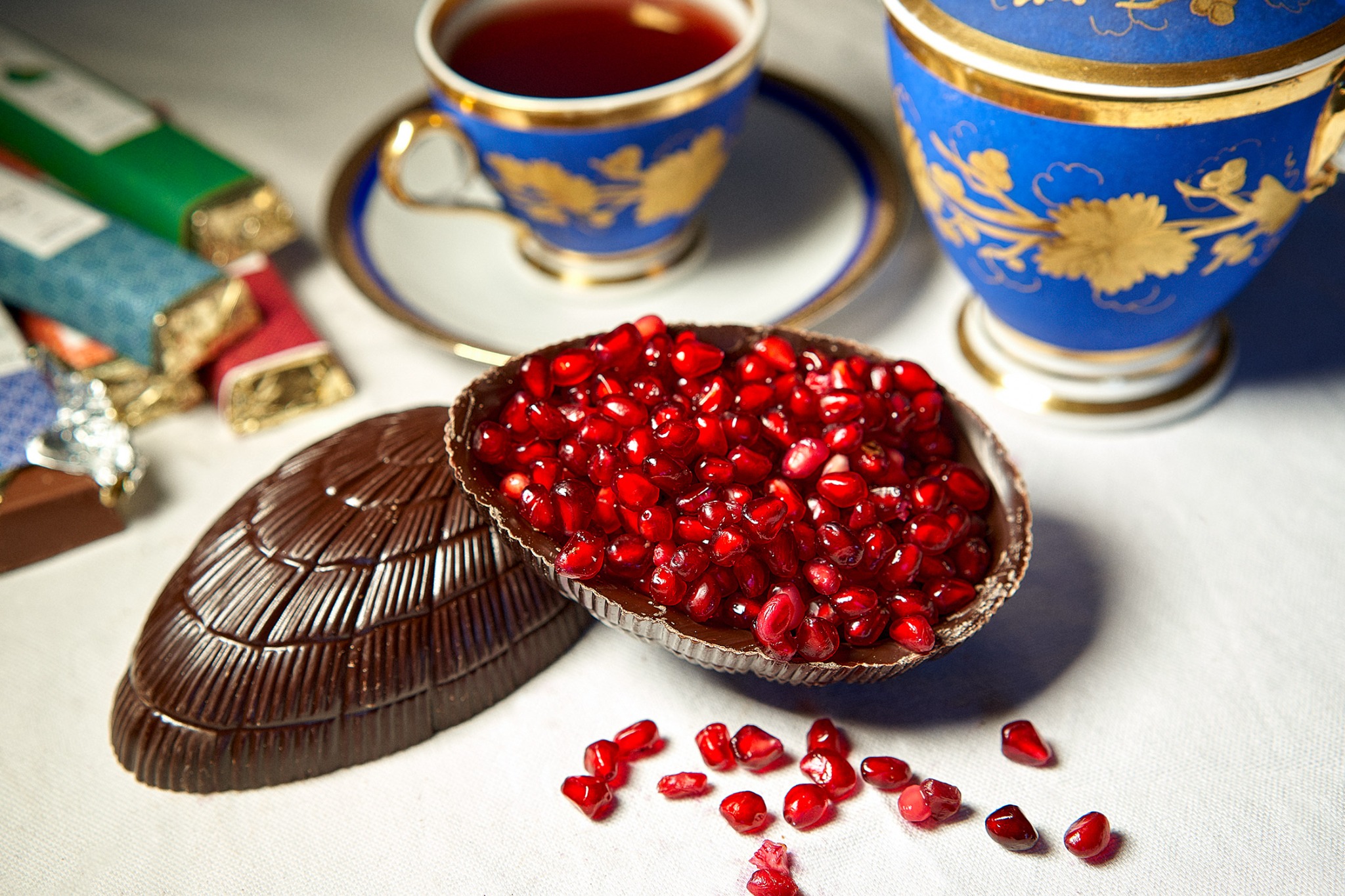 Œuf en chocolat garni de grenade à côté de tasses bleues.
