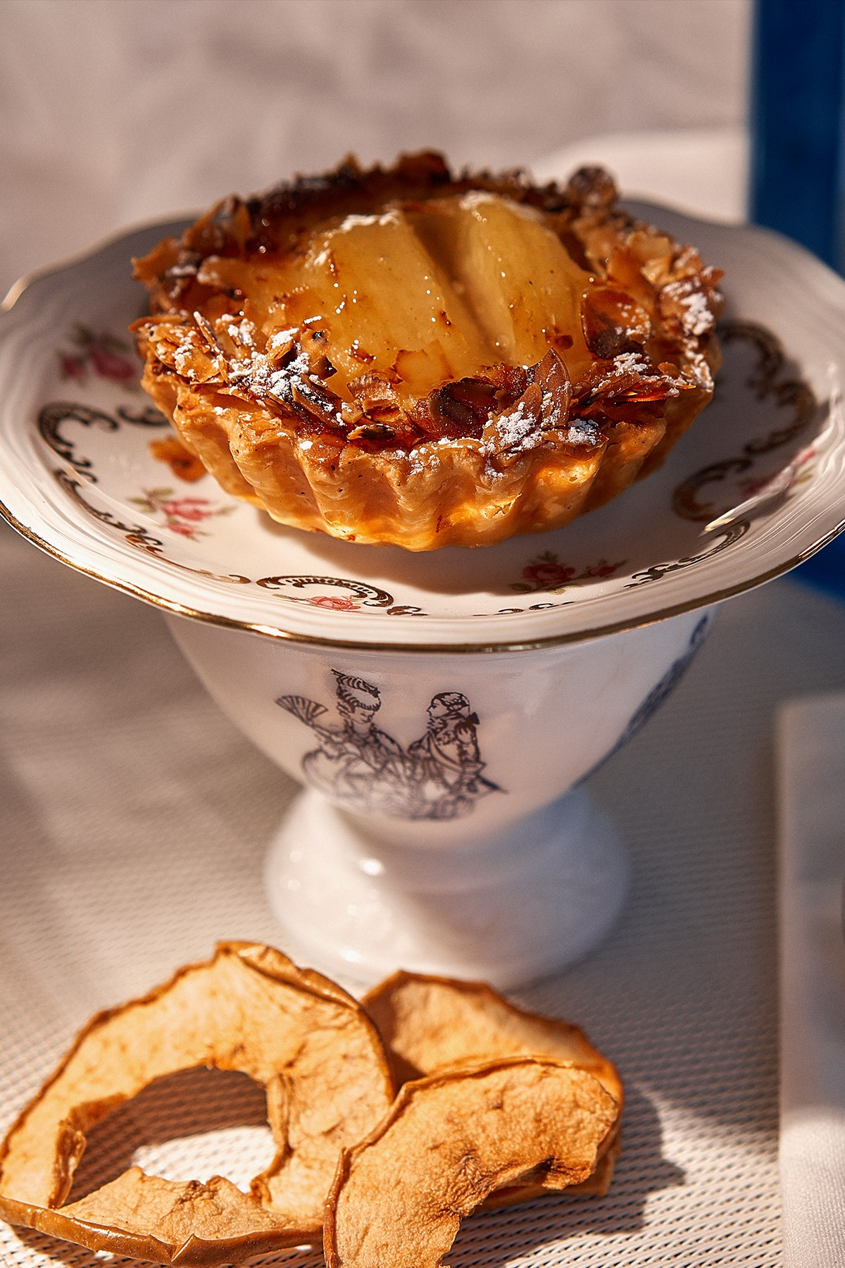 Tartelette aux poires servie sur une pièce de vaisselle ancienne.